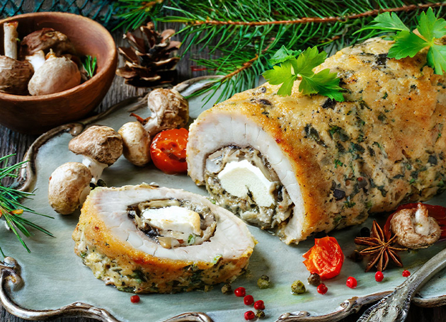 Eine Roulade mit Pilzen und Fisch auf einem Servierplatte. Im Hintergrund sind Pilze und Baumnadeln