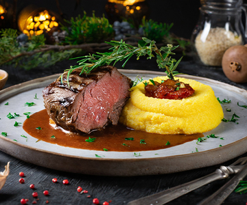 Ein Teller mit einem Rindsbraten, Sauce und und Polentapürre.