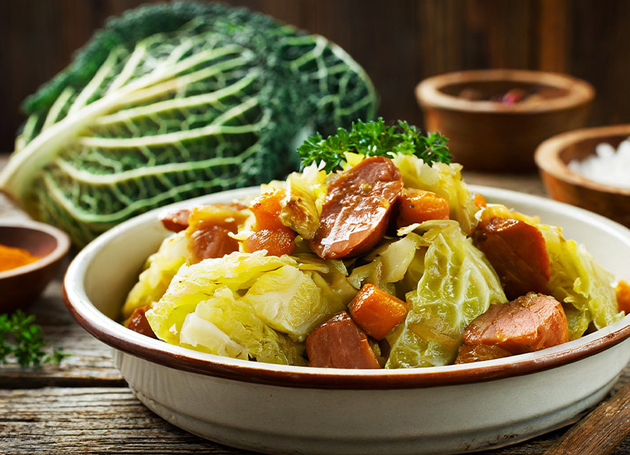 Eine Schüssel mit Wirz-Stücken und Wurst auf einem Holztisch.