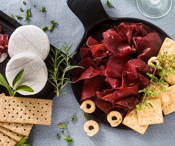 Zwei Platten mit Carpaccio, Camemebert und Crackern auf einem Tisch.