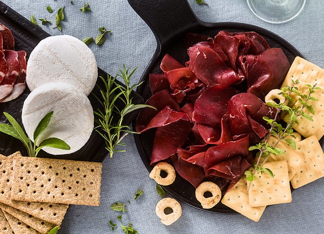 Zwei Platten mit Carpaccio, Camemebert und Crackern auf einem Tisch.