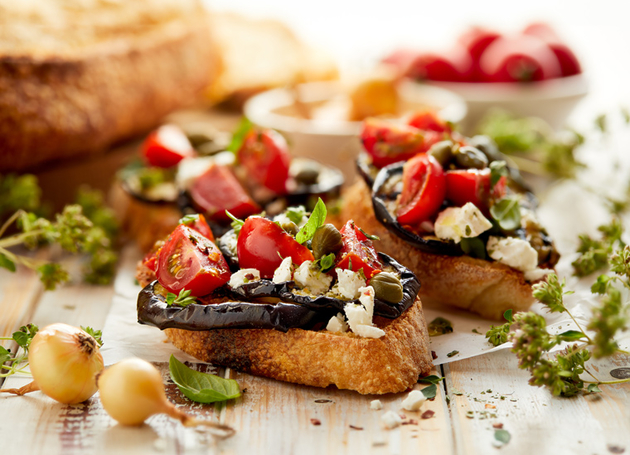 Ein Teller mit Bruschetta mit Tomaten, Auberginen und Kapern darauf.