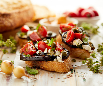 Ein Teller mit Bruschetta mit Tomaten, Auberginen und Kapern darauf.