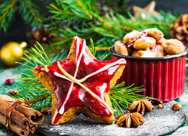 Ein sternförmiger Lebkuchen mit rotem Zuckerguss und auf einem Teller. Im Hintergrund ist eine Schüssel mit weiteren Lebkuchen.