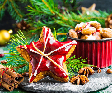 Ein sternförmiger Lebkuchen mit rotem Zuckerguss und auf einem Teller. Im Hintergrund ist eine Schüssel mit weiteren Lebkuchen.