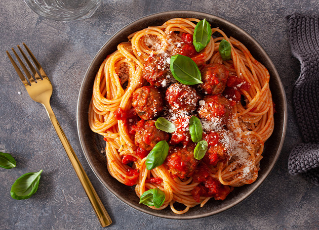 Spaghetti mit Tomatensoße, Fleischbällchen und Basilikum auf einem Teller.