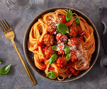Spaghetti mit Tomatensoße, Fleischbällchen und Basilikum auf einem Teller.