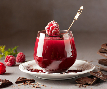 Ein Glas mit Himbeerkompott mit Schokolade. Das Glass ist mit einer gefrorenen Himbeere dekoriert. 