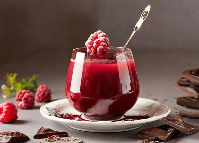 Ein Glas mit Himbeerkompott mit Schokolade. Das Glass ist mit einer gefrorenen Himbeere dekoriert. 