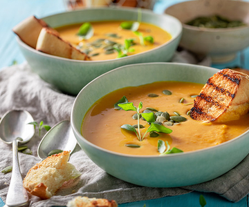 Zwei Schüsseln mit Kürbiscremesuppe mit gegrilltem Brot oben drauf.