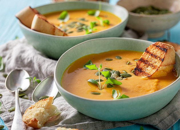 Zwei Schüsseln mit Kürbiscremesuppe mit gegrilltem Brot oben drauf.