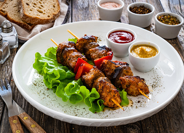 Kalbfleisch Spiesse mit Kopfsalat garniert und mit verschiedenen Sossen in kleinen Schüsseln..