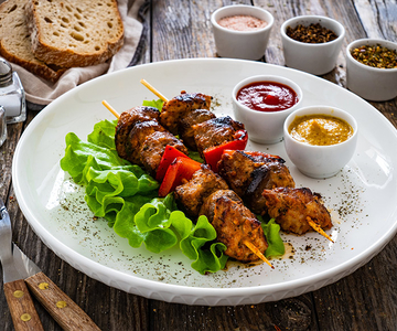 Kalbfleisch Spiesse mit Kopfsalat garniert und mit verschiedenen Sossen in kleinen Schüsseln..