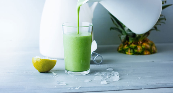 Ein grüner Smoothie mit Ananas und Spinat wird in ein Glas gegossen.