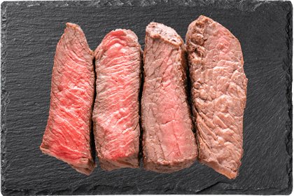 Vier Stücke medium-rare Rindersteak, nebeneinander auf einer dunklen Schieferplatte angeordnet.