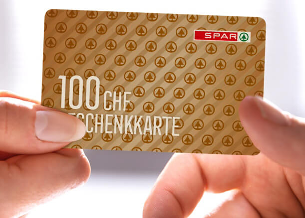 Die Frau hält eine goldene SPAR-Geschenkkarte über 100 CHF.